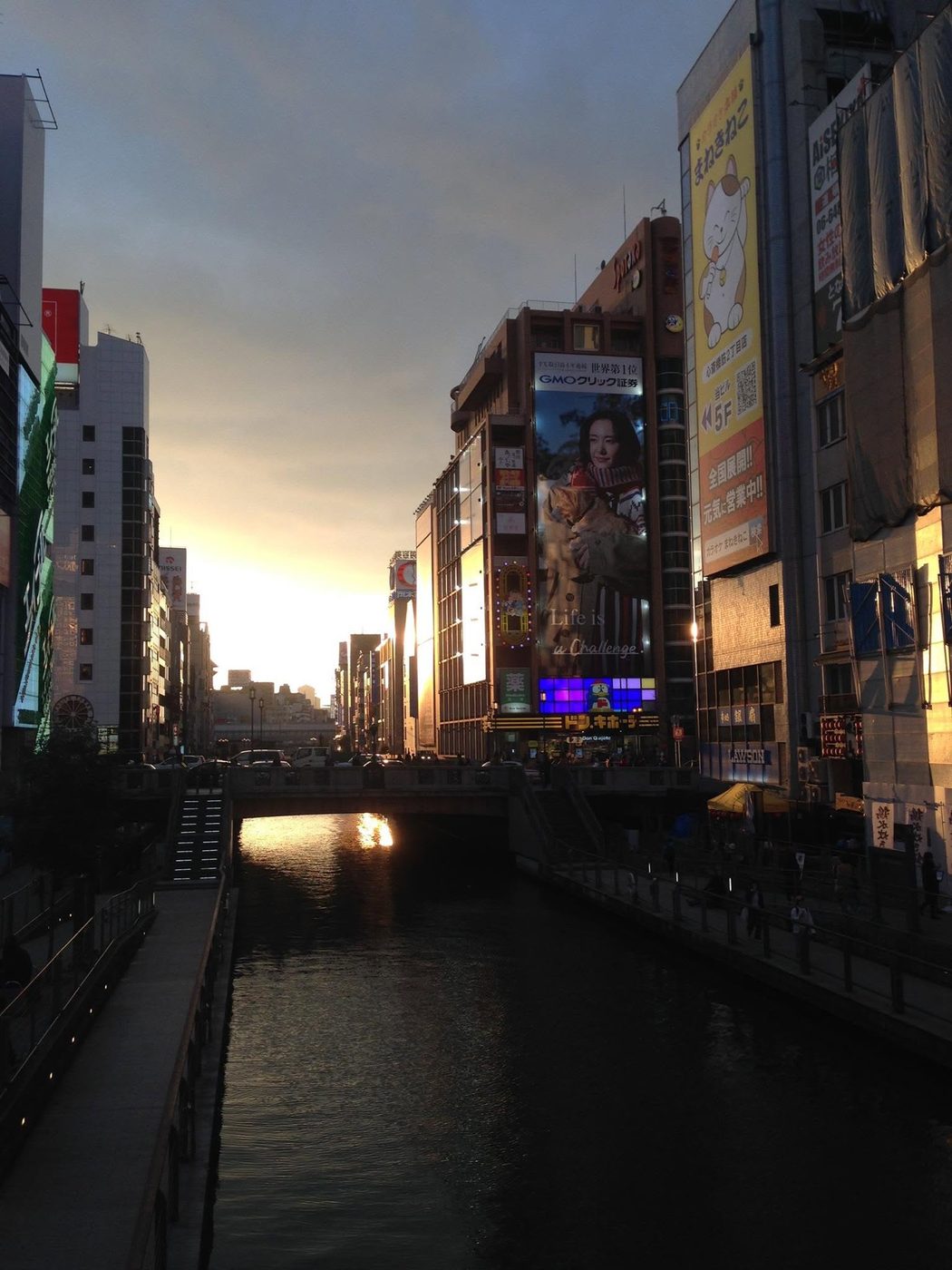 Sun setting down a canal between neon-signed buildings in Osaka