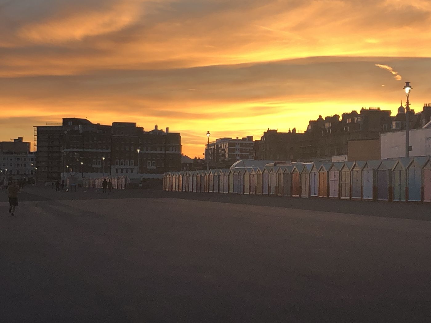 Beach huts along Brighton seafront under a blazing golden sky